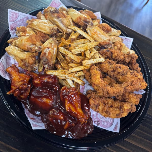 A black platter filled with plain and BBQ chicken wings, crispy tenders, and seasoned french fries.
