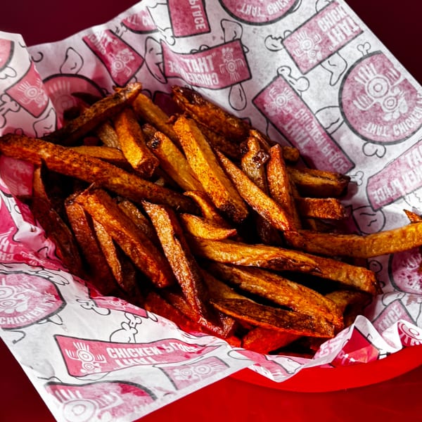 Crispy golden-brown french fries served in a red basket with chicken-themed branded paper.