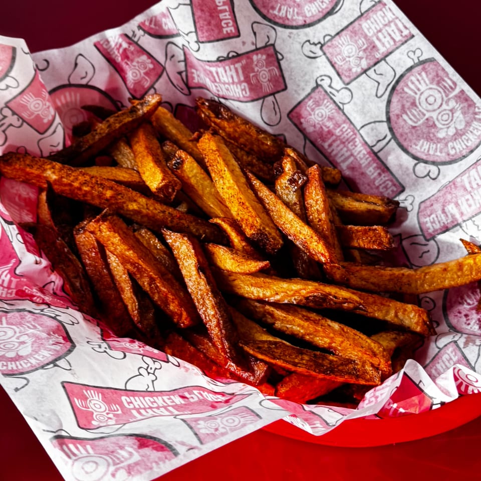 Crispy golden-brown french fries served in a red basket with chicken-themed branded paper.