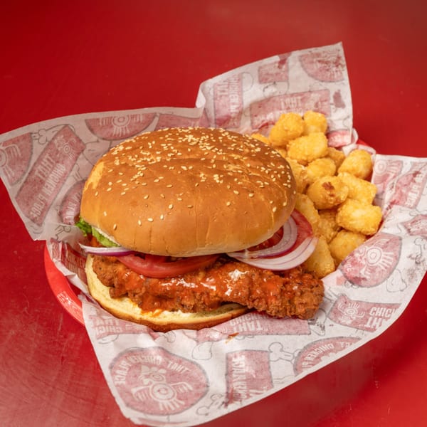 That Chicken Place's fried chicken sandwich with red sauce, tomato, onion, and tater tots.