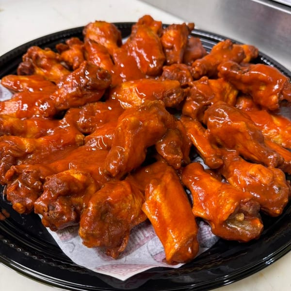A black platter filled with numerous That Chicken Place fried chicken wings coated in a vibrant red sauce.