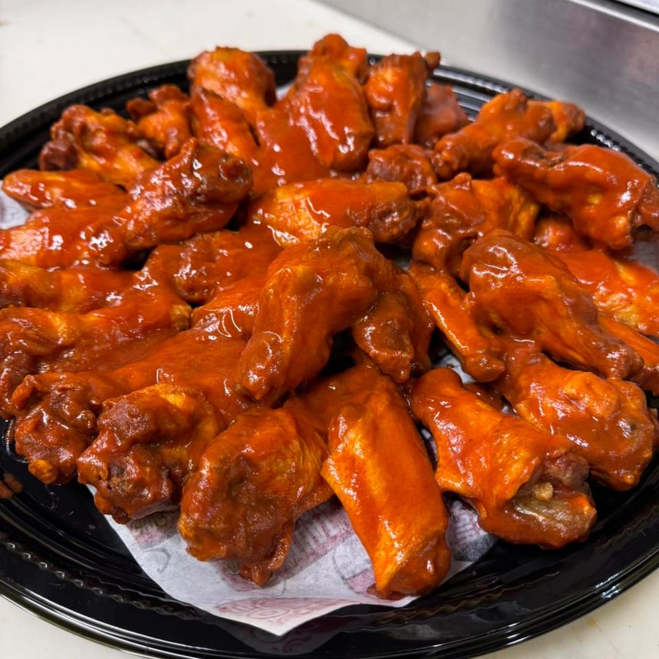 A black platter filled with numerous That Chicken Place fried chicken wings coated in a vibrant red sauce.