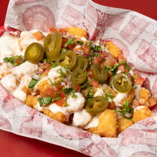 Loaded tater tots with cheese sauce, pico de gallo, and jalapeños in a red basket.