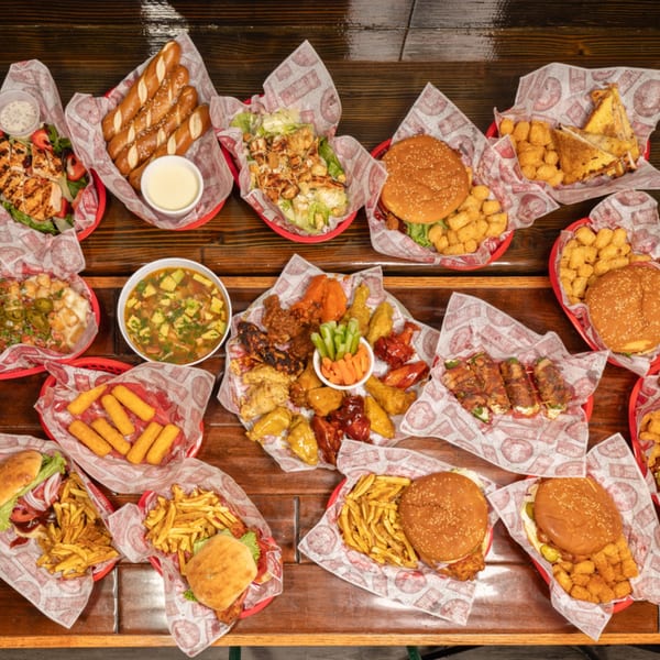 Overhead shot of a wooden table showcasing a large spread of burgers, wings, salads, and appetizers.