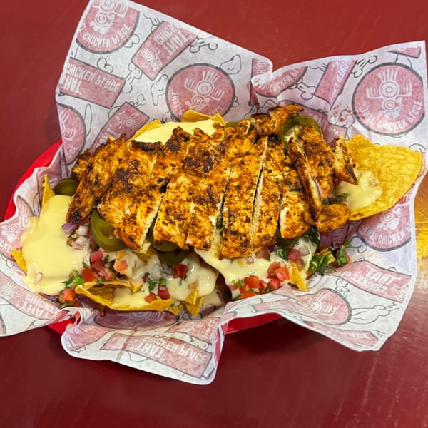 Loaded nachos from TAHT CHICKEN BRUCE with grilled chicken, cheese, pico, and jalapeños in a red basket.