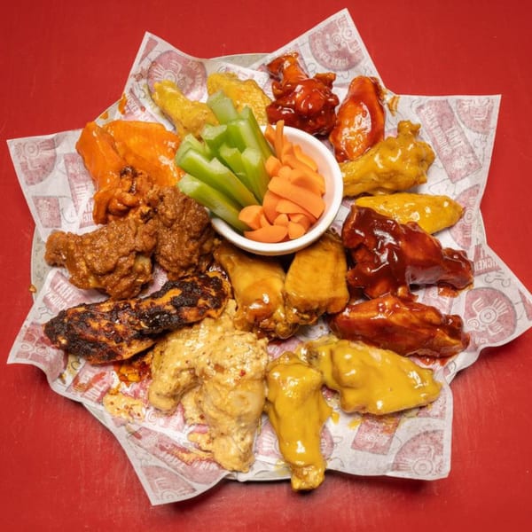 A platter of That Chicken Place wings in various flavors with celery and carrots.