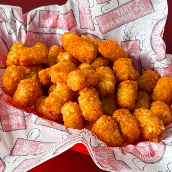 Golden-brown seasoned tater tots in a red basket lined with branded paper.