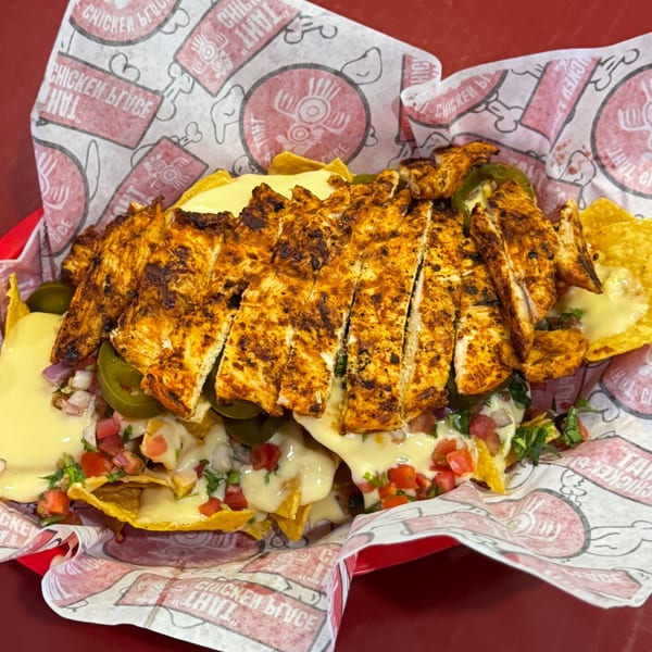 Grilled chicken nachos with melted cheese, pico de gallo, and jalapeños in a red basket.
