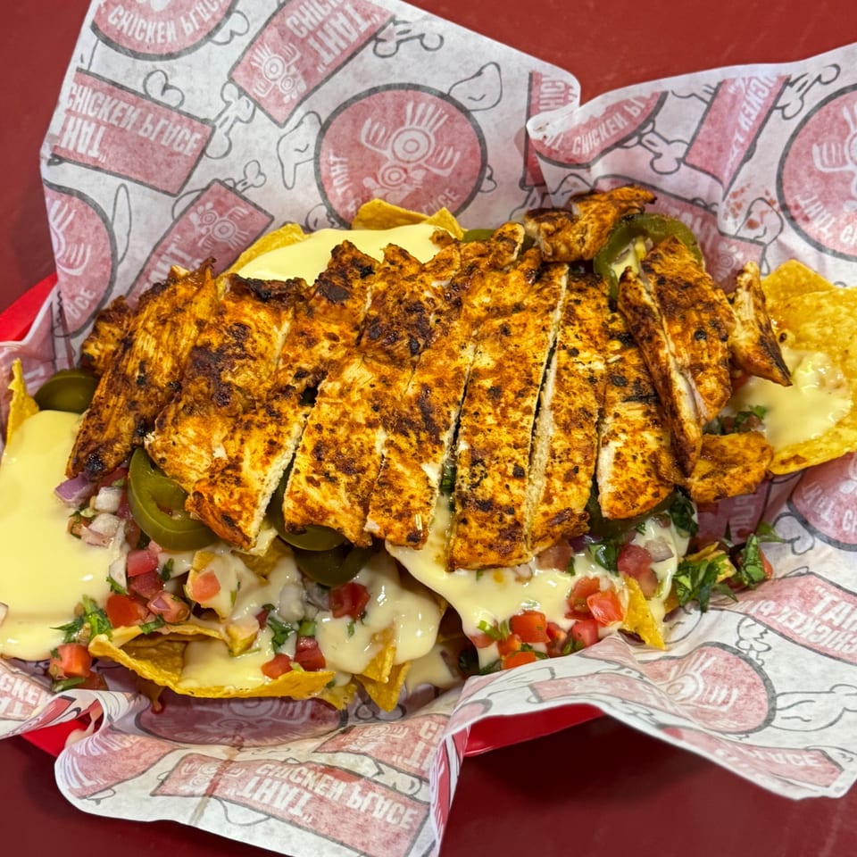 Grilled chicken nachos with melted cheese, pico de gallo, and jalapeños in a red basket.