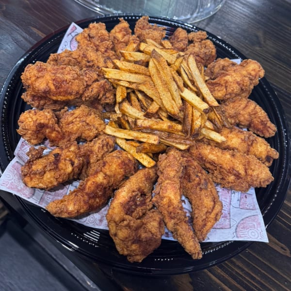 Platter of crispy fried chicken tenders and seasoned french fries on a black tray.