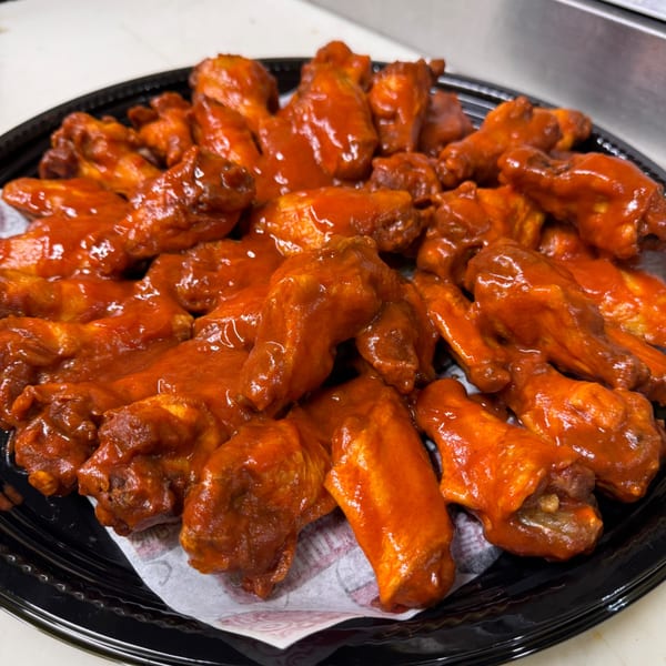 Many chicken wings coated in a vibrant red sauce on a black serving platter.