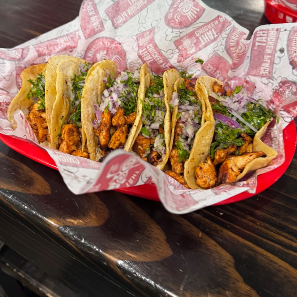 Six chicken tacos topped with red onion and cilantro in a red basket on a wooden table.